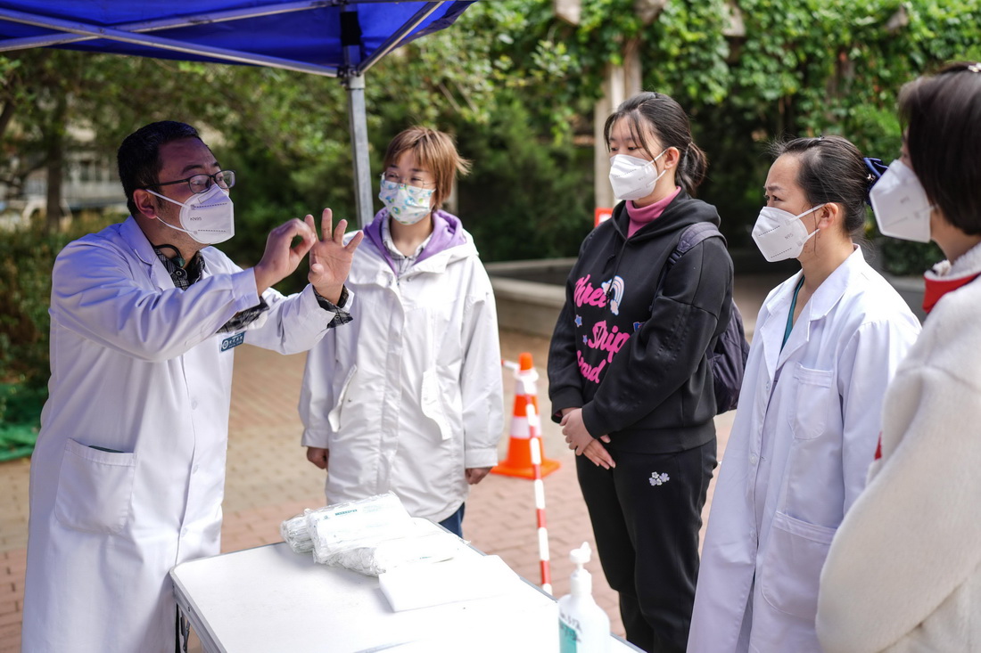 5月11日，在西城區白紙坊街道一處社區核酸採樣點，宣武醫院帶隊醫生王長明（左一）向同事講解核酸採樣時的注意事項。新華社記者 彭子洋 攝