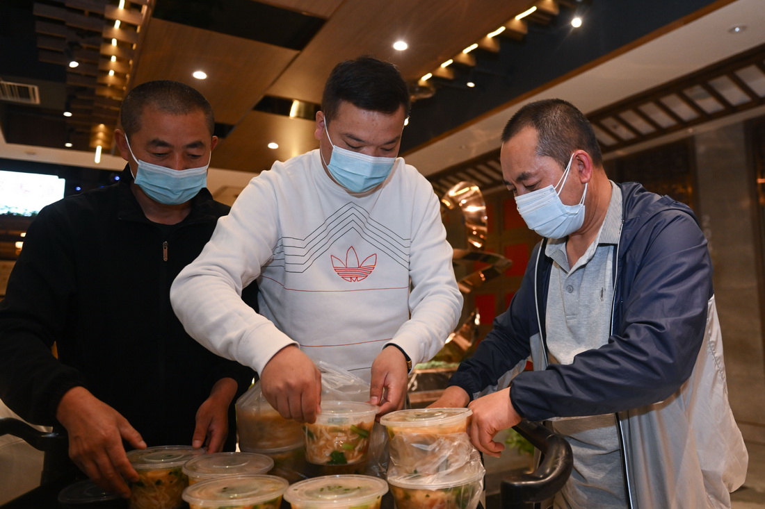 5月19日，朱希明（右）在餐馆门口为取餐的疫情防控工作人员帮忙。新华社记者 张龙 摄