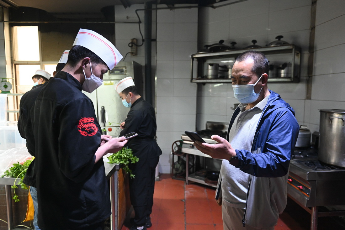 5月19日，朱希明（右）在自家餐馆里与厨师核对当天要送的盒饭数量。新华社记者 陈杰 摄