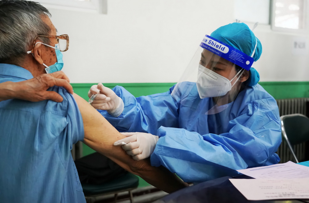 6月20日，在学院路街道六道口社区的一处新冠疫苗临时接种点，医护人员（右）为小区居民接种新冠疫苗。