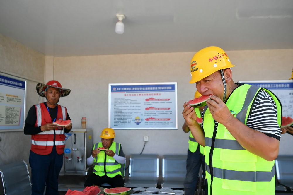 6月23日，在陝西西咸新區世紀大道提升改造工程施工現場，中鐵二十局工人在工作間隙品嘗西瓜。