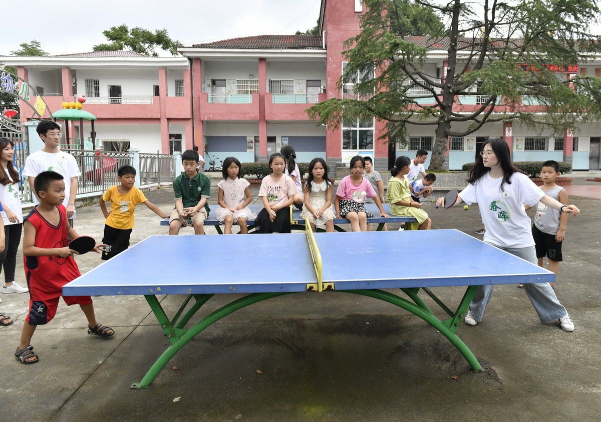 在江西省南昌市灣裡管理局羅亭鎮義坪小學，大學生志願者和留守兒童在打乒乓球（7月19日攝）。