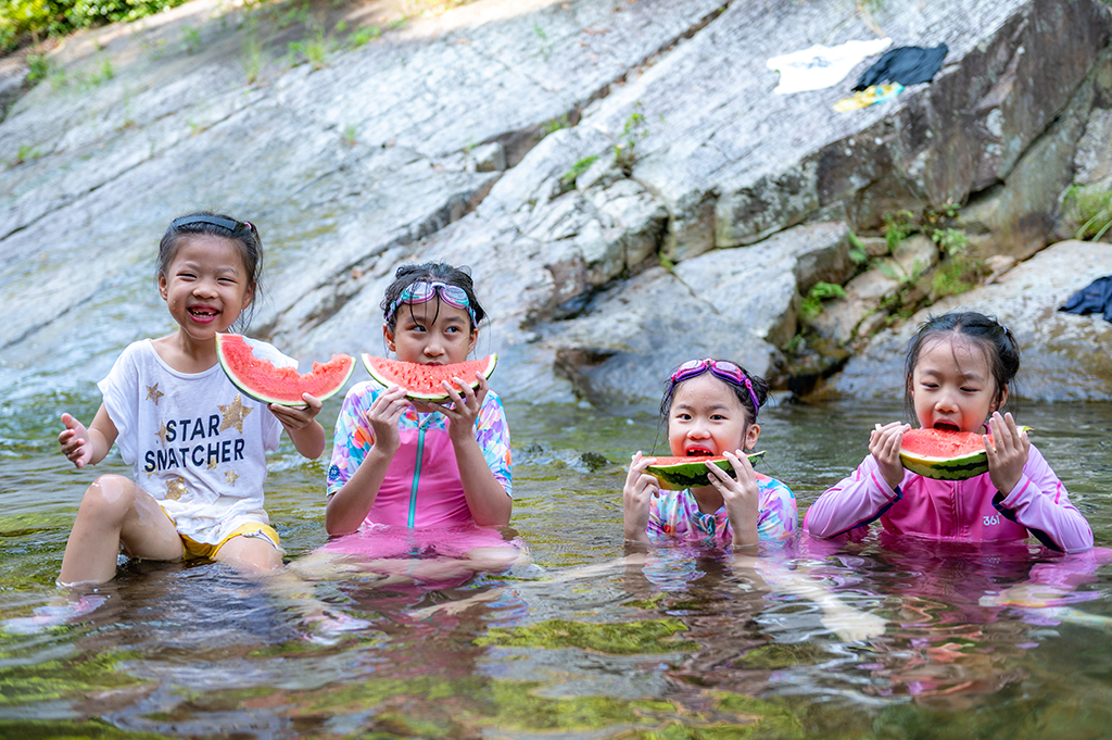 广西各地持续高温，小朋友在南宁市武鸣区的一条河谷里吃西瓜消暑。人民网 严立政摄