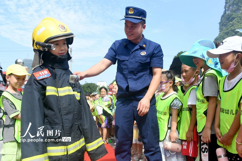 2022年8月8日，在广西河池市罗城仫佬族自治县消防救援大队，消防员指导孩子们试穿和体验消防服套装。