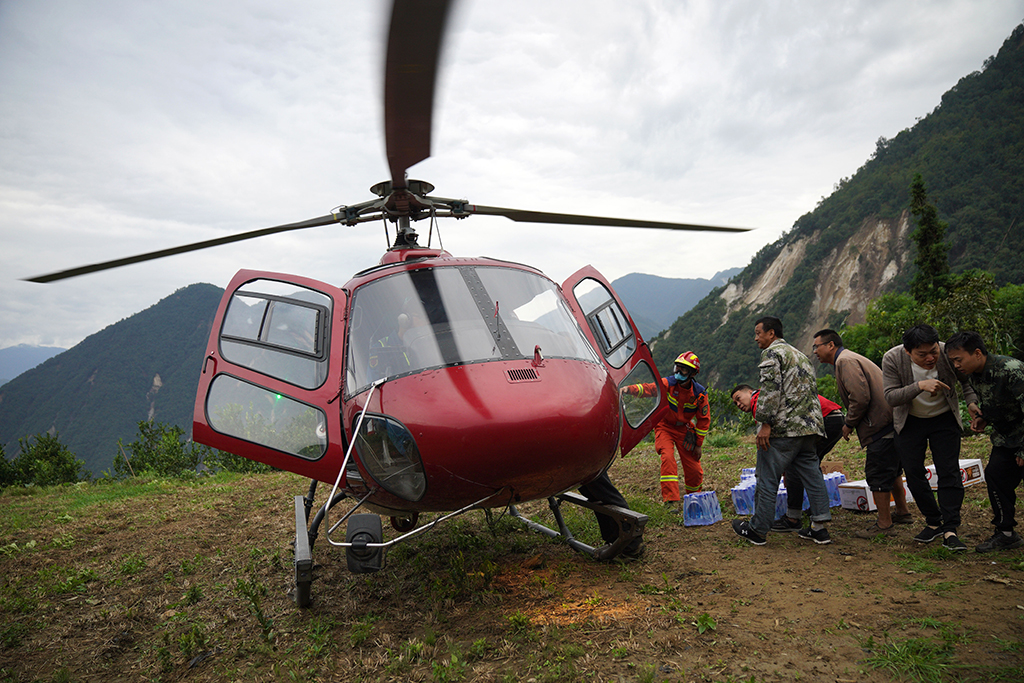 9月7日，在雅安市石棉县王岗坪彝族藏族乡幸福村二组，村民与消防救援队员搬运直升机送来的水和食物。