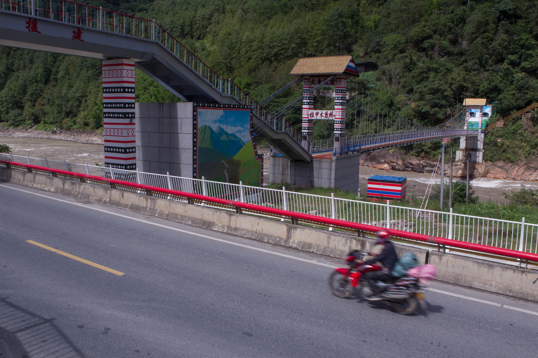 2022年9月14日，怒江州福貢縣拉甲木底村居民駕駛摩托車從拉甲木底橋下駛過。這座橋將過街天橋和過江橋梁相結合，方便行人過江、過街。新華社記者 岑雲鵬 攝