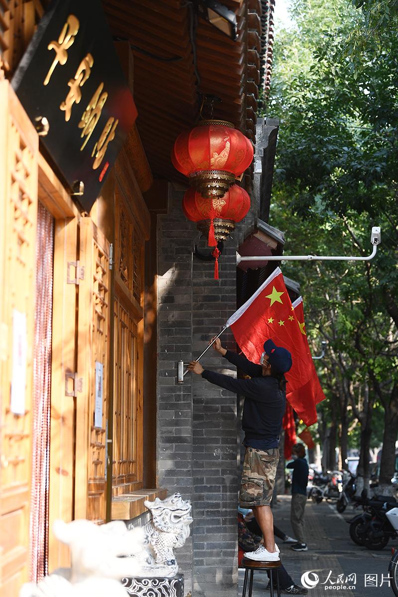 9月30日，在北京西兴隆街，临街商家工作人员正在悬挂国旗迎接国庆的到来。人民网记者 于凯摄