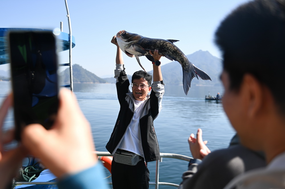 10月22日，在浙江省淳安县千岛湖黄山尖水域，游客用双臂举起刚捕获的“鱼王”。