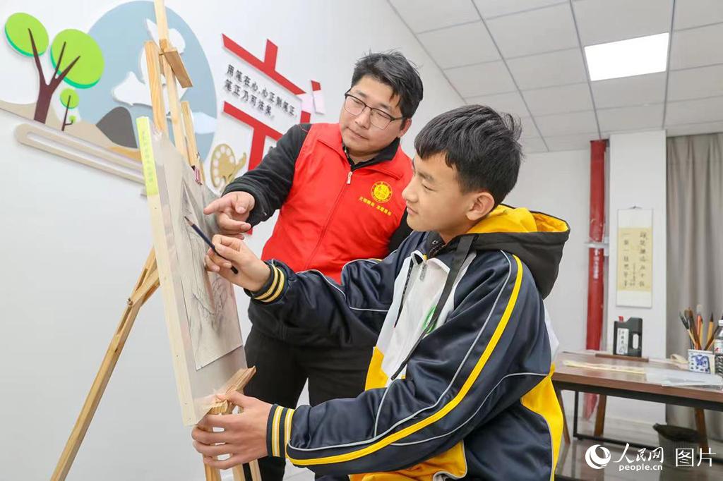 11月18日，在盱眙縣鮑集鎮朱巷村委會，志願者楊亮為薛之寒上繪畫課。