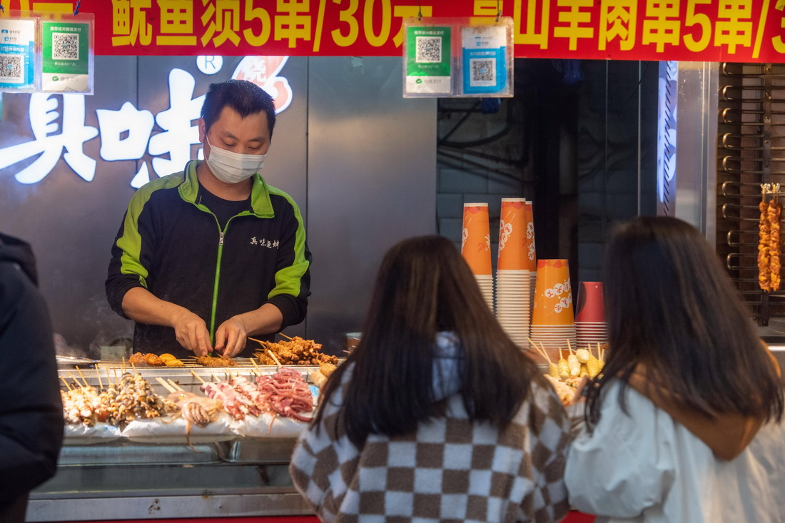12月23日，在位於重慶解放碑商圈的八一路好吃街上，商家為顧客制作小吃。