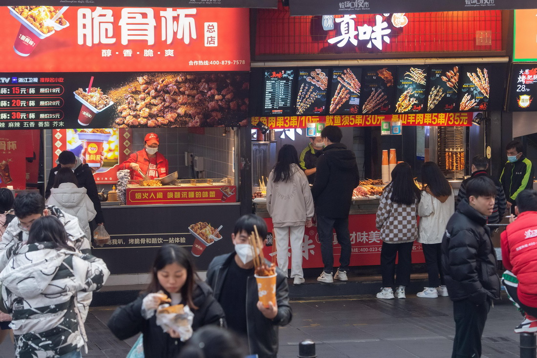 12月23日，在位於重慶解放碑商圈的八一路好吃街上，市民游客挑選小吃美食。
