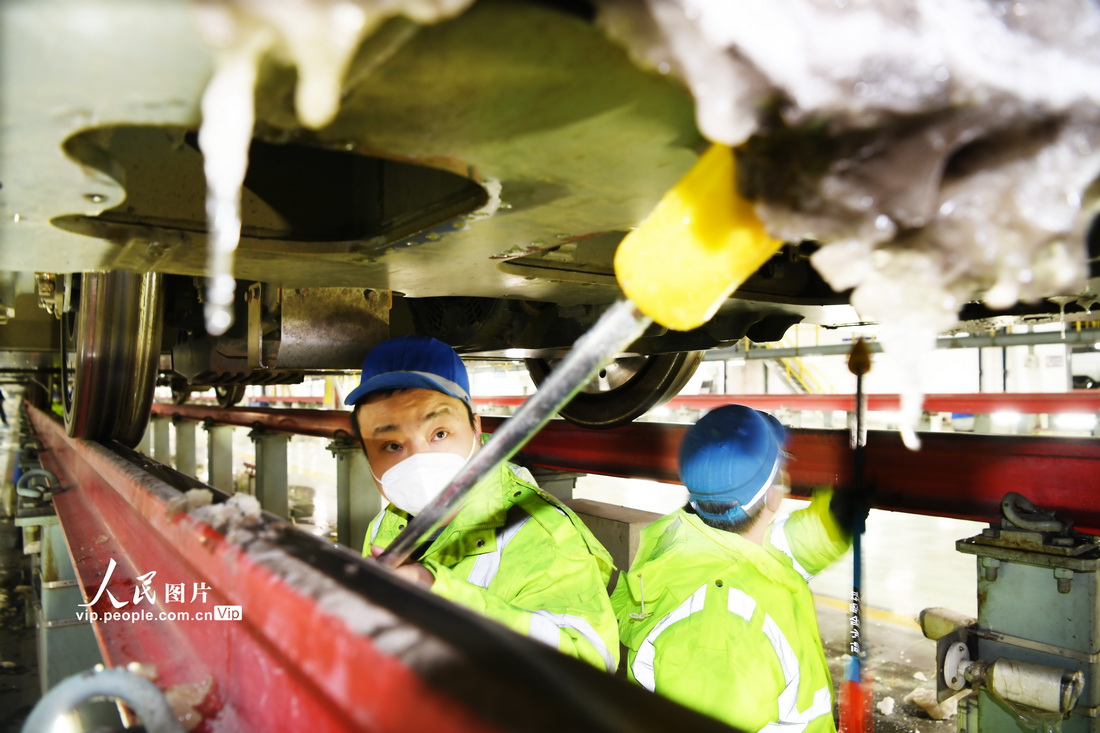 1月14日晚，郑州动车段动车组机械师在检修库对动车车底进行融冰除雪作业。