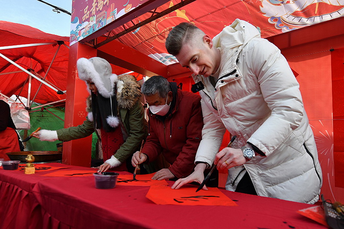 1月15日，在山東省青島市城陽區的一場年貨節活動上，一名外國游客（右）體驗中國傳統書法。新華社發（王海濱 攝）