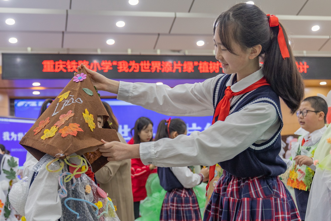 3月10日，重庆市九龙坡区铁路小学的一名学生在同学的帮助下穿戴自己制作的环保服装。
