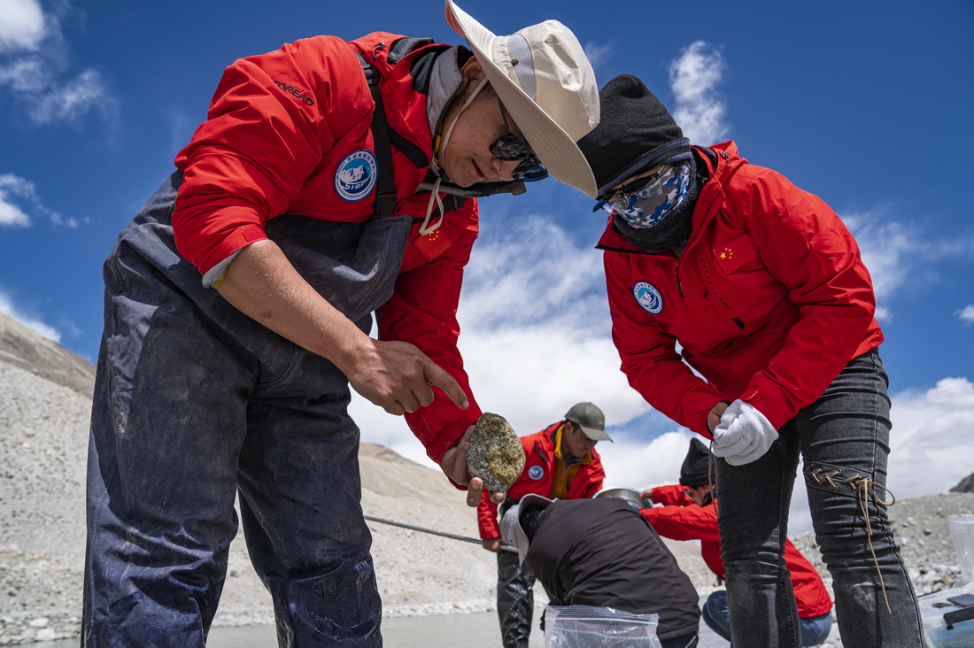 在珠峰登山大本营附近，来自西藏大学生态环境学院的科考队员张继峰（左）在查看附着在石头上的藻类生物（5月22日摄）。新华社记者 孙非 摄