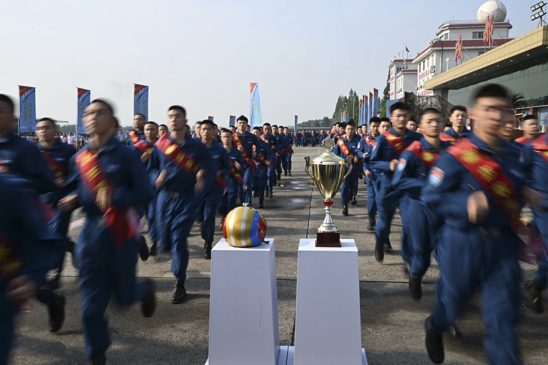 7月19日，在成都某軍用機場，空軍新錄取飛行學員跑步經過“金頭盔”和“航空飛鏢”獎杯。新華社發（余紅春 攝）