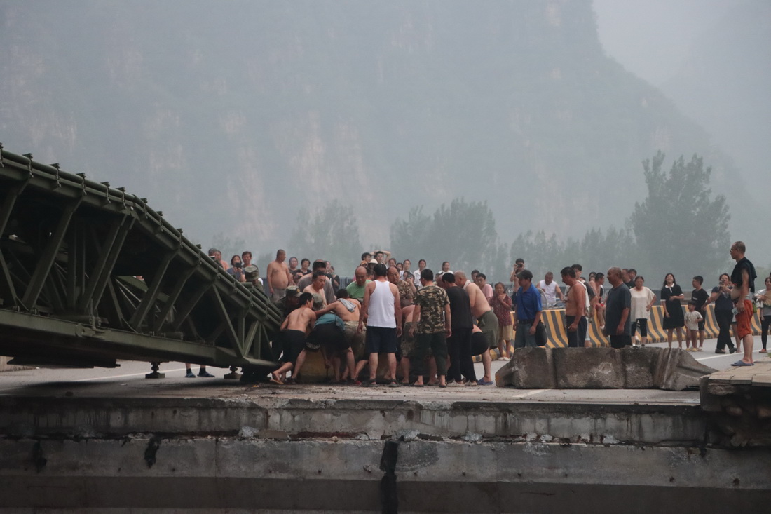 8月3日，中部战区陆军第82集团军某旅官兵在北京市房山区涞宝路四渡桥断桥处架设桥梁时，当地群众帮助移除障碍物。新华社发（张康 摄）