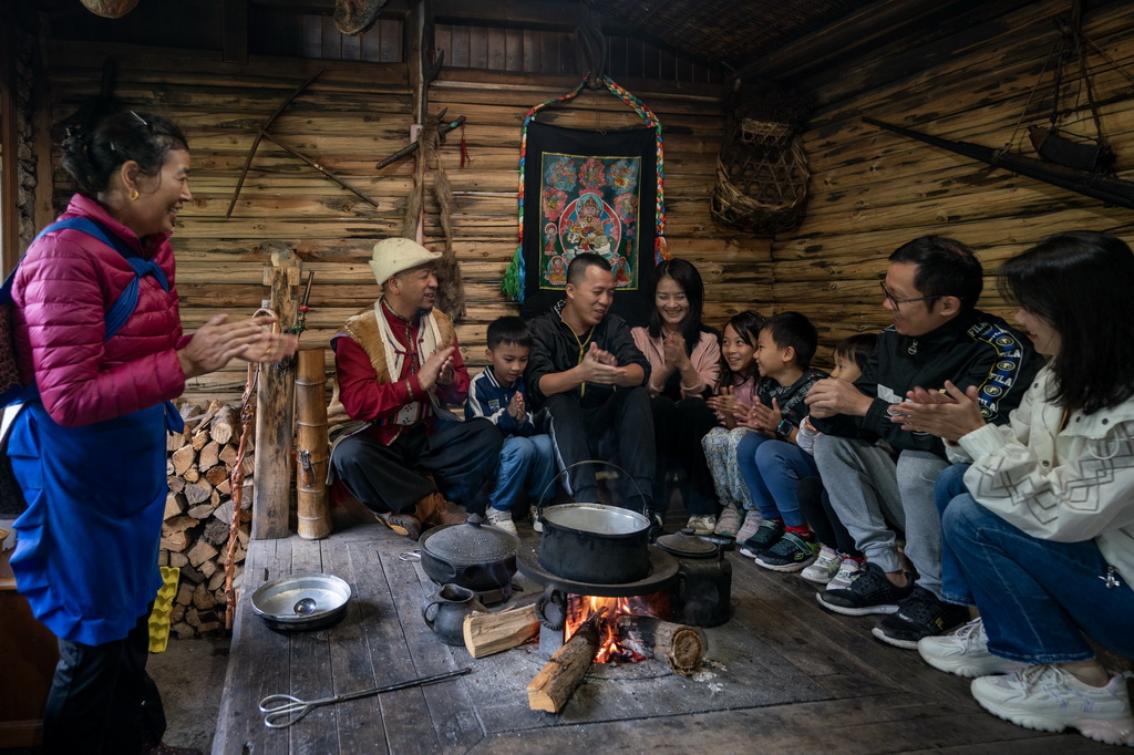 麗江市玉龍納西族自治縣白沙鎮玉湖村村民和杰林（左二）和妻子（左一）在火塘邊帶著游客唱納西族歌曲（8月28日攝）。