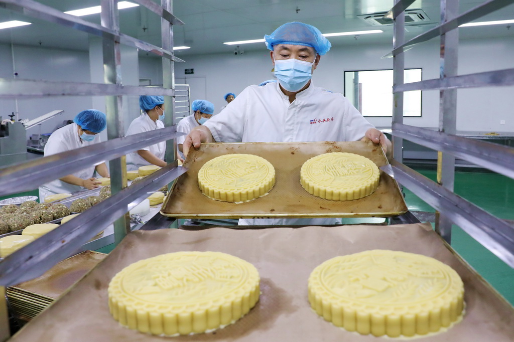 9月13日，在山東省青島西海岸新區一家月餅生產企業，工人將制作好的大月餅放到烤架上。新華社發（王培珂攝）