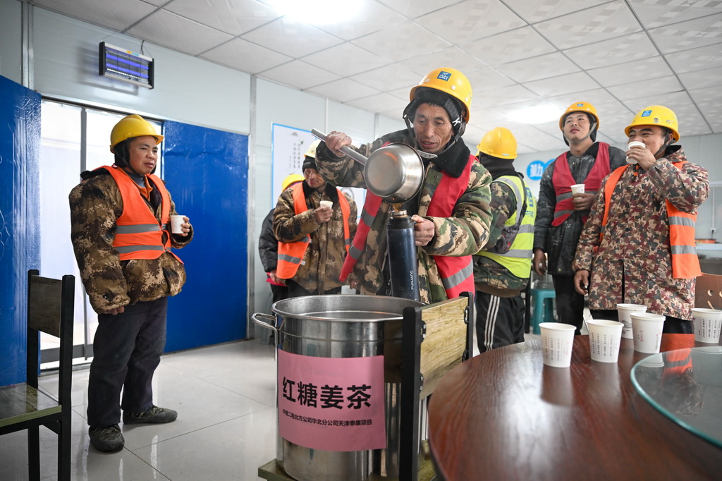  12月12日，在中建二局北方公司天津泰康項目工地，工人在飲用為他們准備的紅糖姜茶驅寒。新華社記者 孫凡越 攝