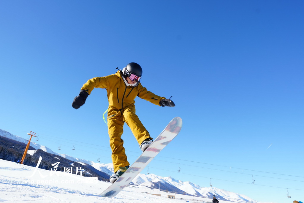 12月16日，一位滑雪愛好者在新疆哈密豫哈鬆樹塘滑雪場玩單板時跳躍起來。