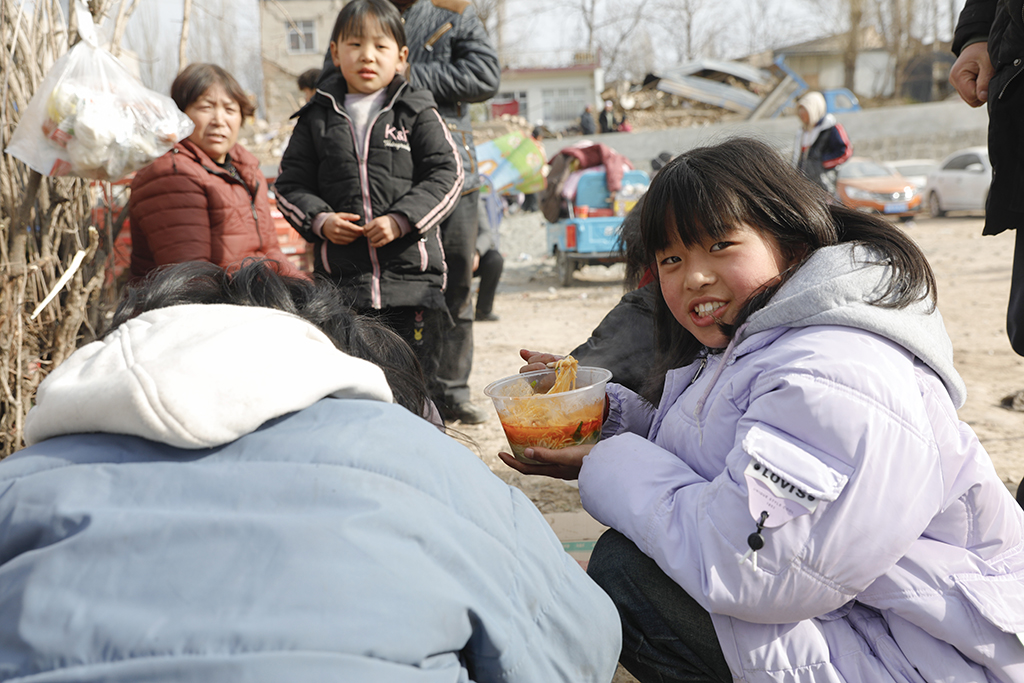12月19日，在甘肅臨夏積石山縣大河家鎮大河村安置點，小朋友在吃愛心牛肉面。新華社記者 方欣 攝