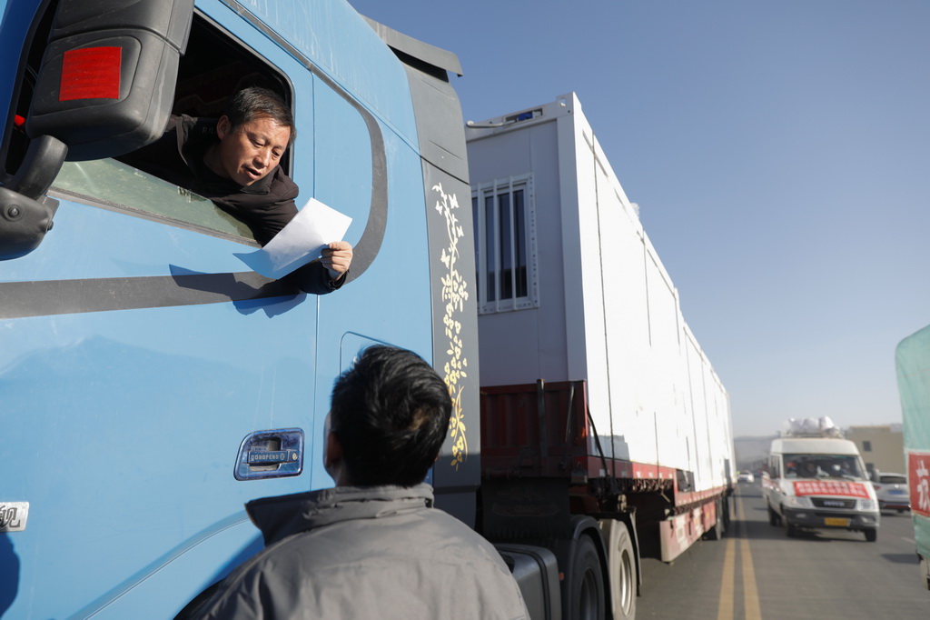 12月26日，在积石山高速出口，马明（下）和另一驰援灾区的卡车司机交流。新华社记者 方欣 摄