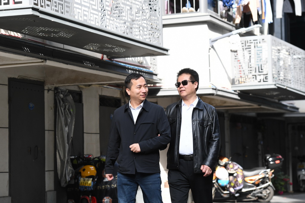 王永澄（右）在志願者的協助下前往福州市鼓樓區紅牆巷小區調研盲人家庭子女入學及保障房入住情況（2月18日攝）。