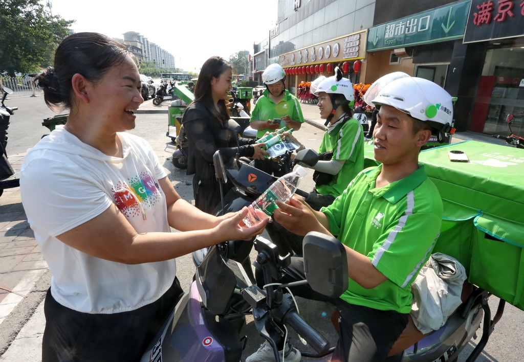 6月18日，北京市丰台区南苑街道的工作人员在街头为餐饮配送员送上冰镇矿泉水等。新华社记者 李欣 摄