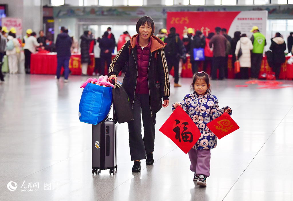 2025年春运首日，书法家在南昌火车站候车大厅内为乘客写“福”字和春联，小乘客展示领取到的“福”字。人民网记者 时雨摄