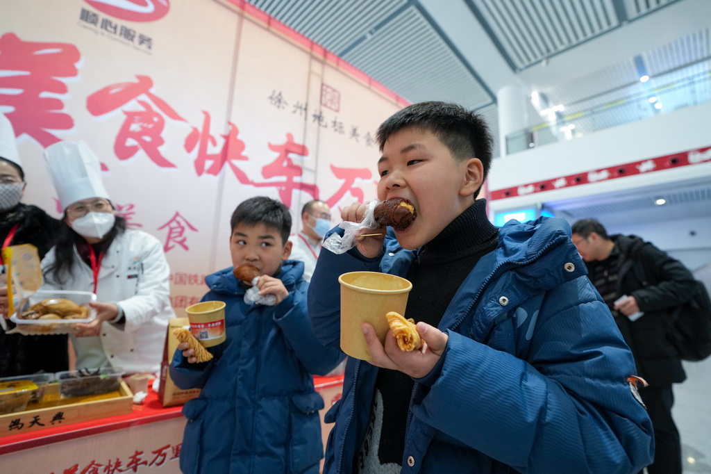 1月22日，两名小旅客在高铁徐州东站候车大厅品尝徐州当地美食。