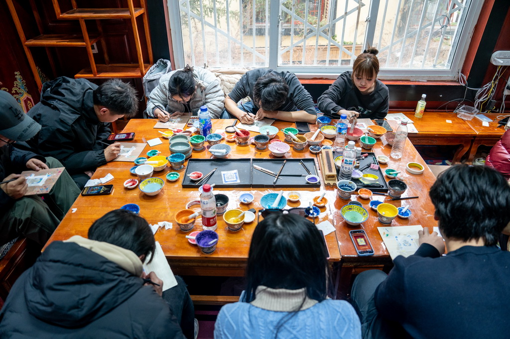 在雲南省迪慶州香格裡拉市獨克宗古城金龍社區非遺體驗中心，游客體驗繪制唐卡（2025年3月6日攝）。