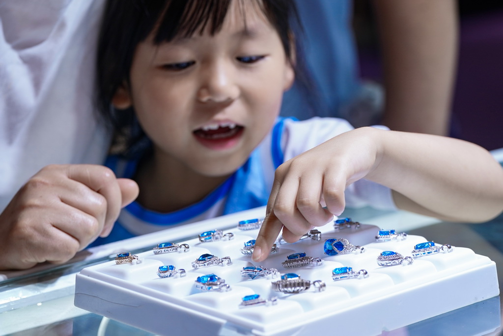 7月10日,小朋友在昆明石博会上帮家长挑选玉石。