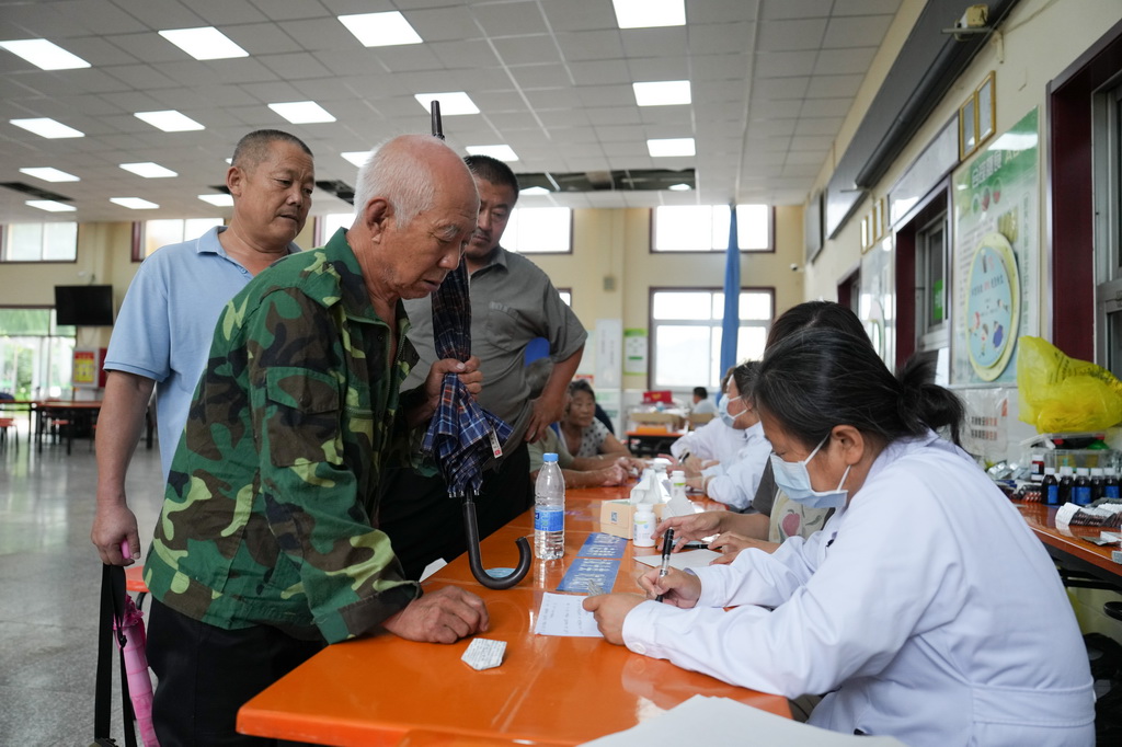 7月29日,在北京市密雲區太師庄中學居民安置點,太師屯鎮社區衛生服務中心的醫生(右)為安置在此的群眾開藥。