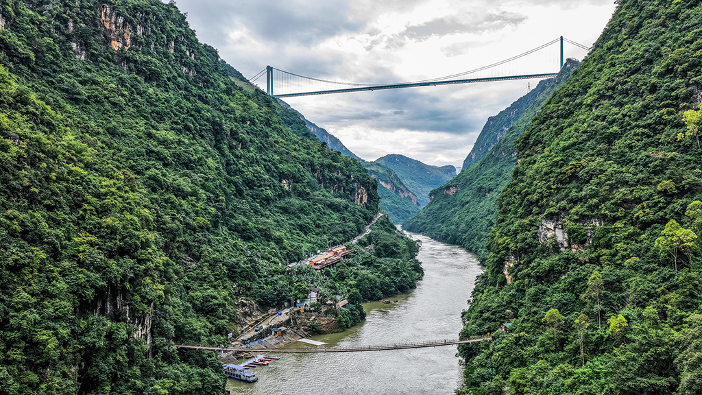 景区内的索道桥与远处的花江峡谷大桥遥相呼应(9月27日摄,无人机照片)。