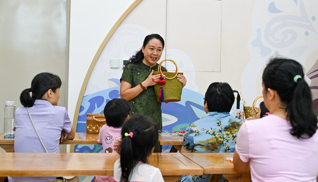 10月12日,在海南省文化馆,东山草编技艺传承人袁洁(后)为家长和小朋友讲解东山草编技艺。