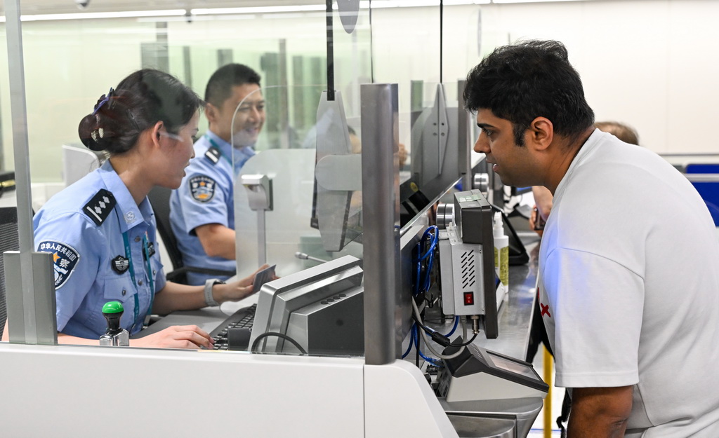 10月15日,在海口美兰边检站,海南2025年第200万名通关外籍旅客卡迪克(右)在办理边检手续。