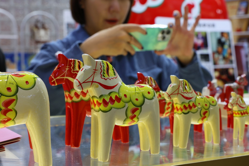 11月7日，在第八届进博会消费品展区，参观者在拍摄一组瑞典传统手工艺达拉木马展品。新华社记者 方喆 摄
