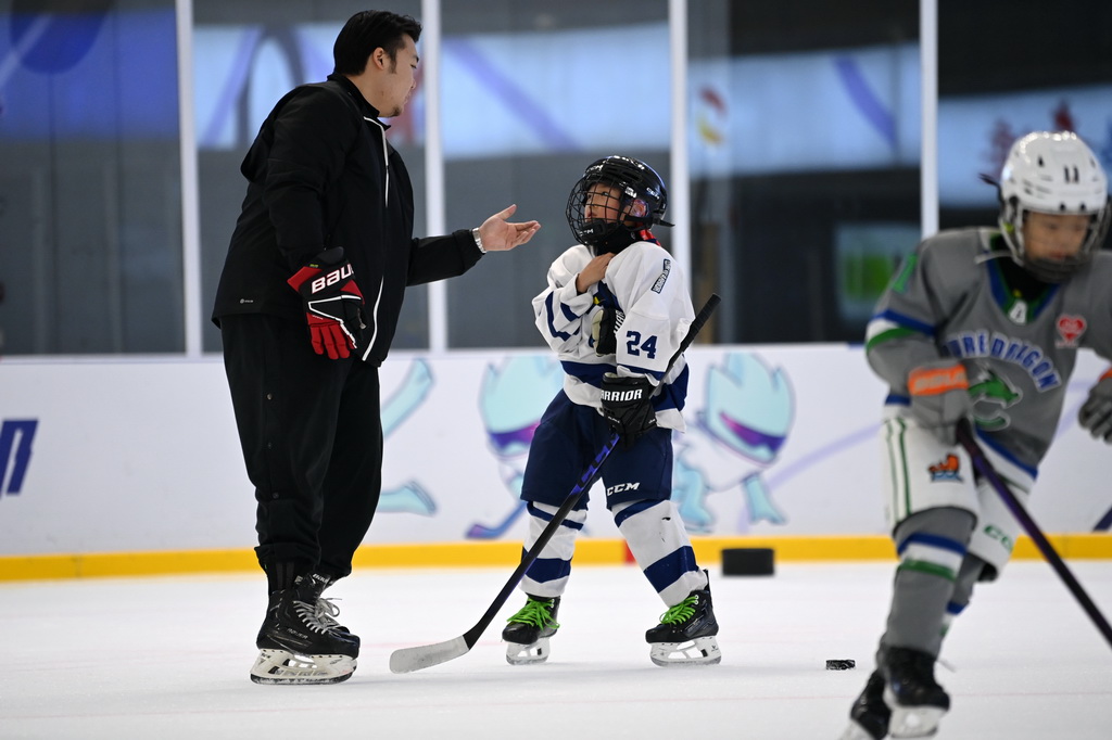 12月3日，冰球教练王恺英（左）在冰上运动公益课上指导小学员。