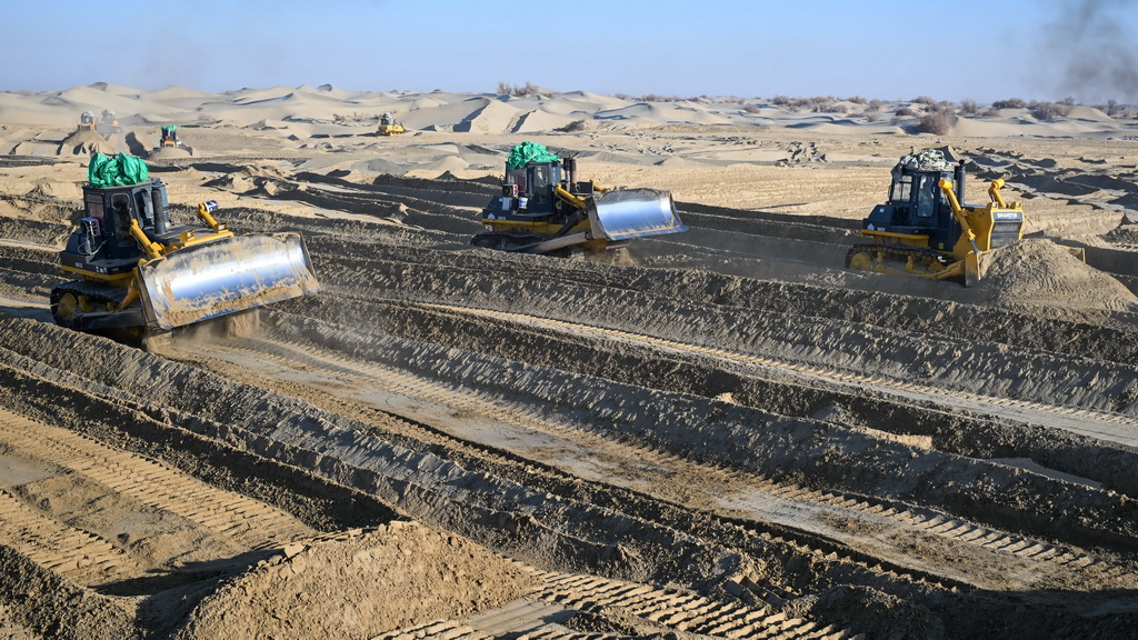 在新疆和田地区墨玉县喀瓦克乡，大型机械在沙漠中穿梭作业、平整沙地（1月11日摄）。