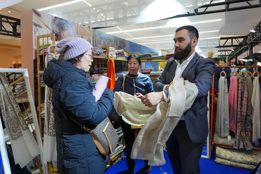 2月4日，在“共享大市場·出口中國”2026年首場活動暨北京國際精品薈的進口商品推介區，參觀者（左）購買展出的烏茲別克斯坦圍巾。