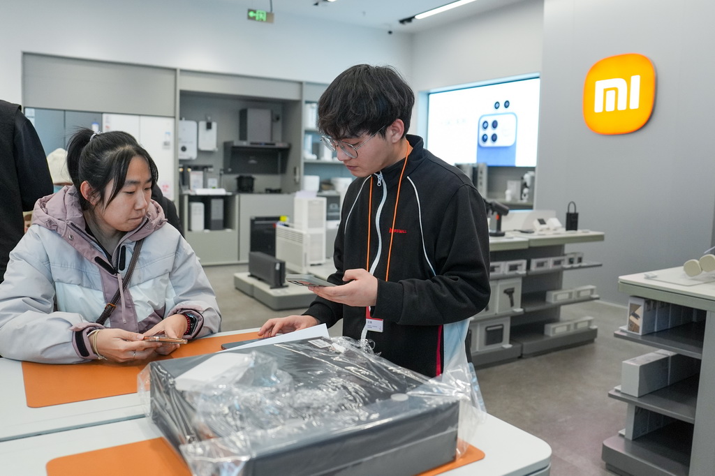 1月9日,在北京京东MALL双井店,一名手机店员工(右)在为使用国补购买手机的消费者核销国补券码。