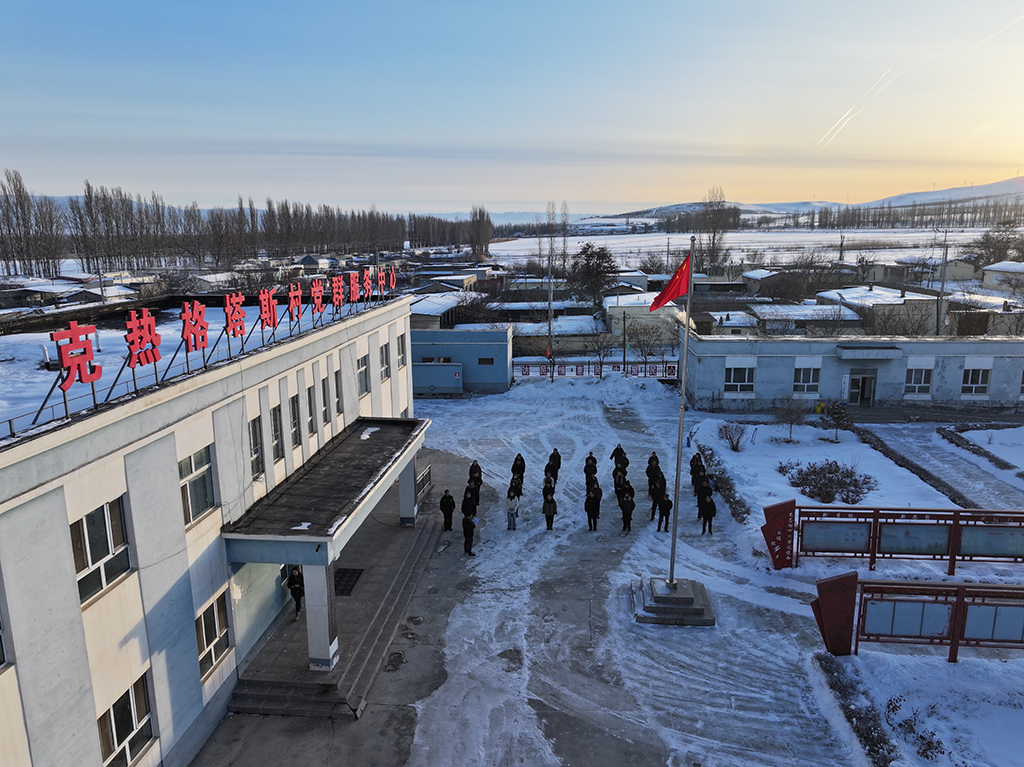 2月9日,在伊犁哈萨克自治州新源县,木沙江·海拉特在克热格塔斯村党群服务中心参加升国旗仪式(无人机照片)。新华社记者 辛悦卫 摄