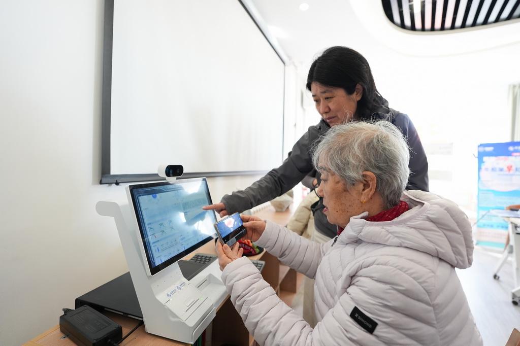 一名社区居民(前)在智慧康养机器人养老驿站内体验一款智慧健康设备(3月18日摄)。