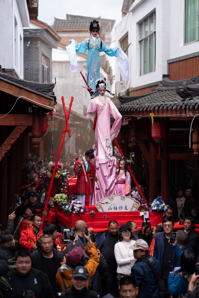 3月20日,四川省兴文县九丝城镇建武村,演员在巡游活动中表演木台铁桩戏《山伯访友》。