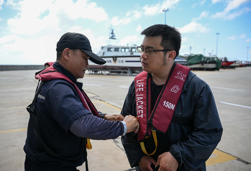 3月19日，海上交通保障船工作人員（左）協助乘客穿戴救生衣。新華社記者 蒲曉旭 攝