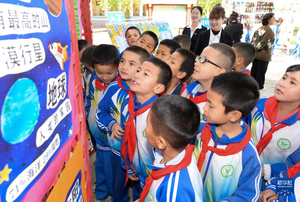 4月21日，在新疆新和县依其艾日克镇木纳尔村小学，小朋友们在“图书巴扎”上阅读书籍海报。