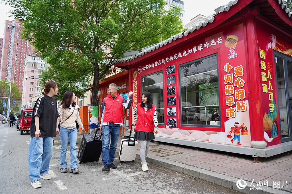 2026年5月17日，志愿者正在帮助游客搬运行李。沈阳小河沿早市已从“马路市场”转型为“网红打卡地+民生服务站”，专门设立了游客服务中心与志愿者服务站，为外地游客开辟了免费行李寄存处，节日期间日均寄存量超200件，且实现零丢失，以暖心服务丰富“烟火经济”新场景。人民网记者周颂雪 摄