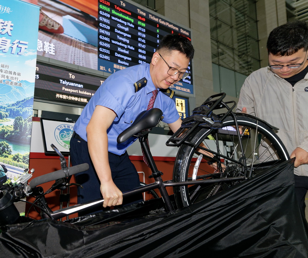 5月19日,工作人员在北京北站检票口处协助将随行自行车放入车站提供的免费装车袋。新华社记者 张笑宇 摄
