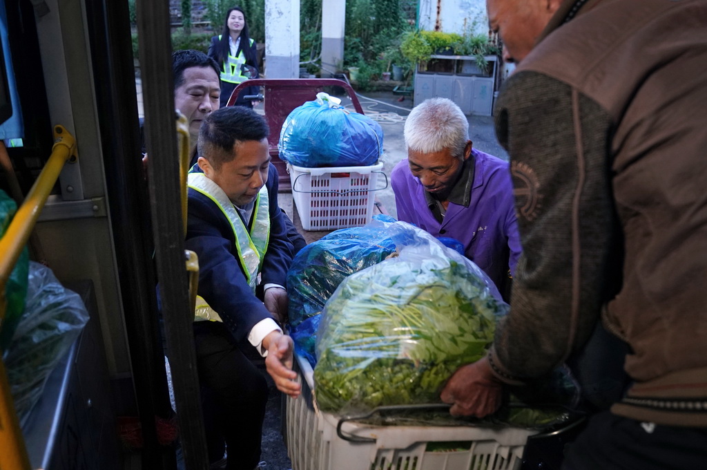 在江西省南昌縣向塘鎮浹溪村的公交站點，公交安全員（左前）協助年長菜農將蔬菜搬上車（5月9日攝）。